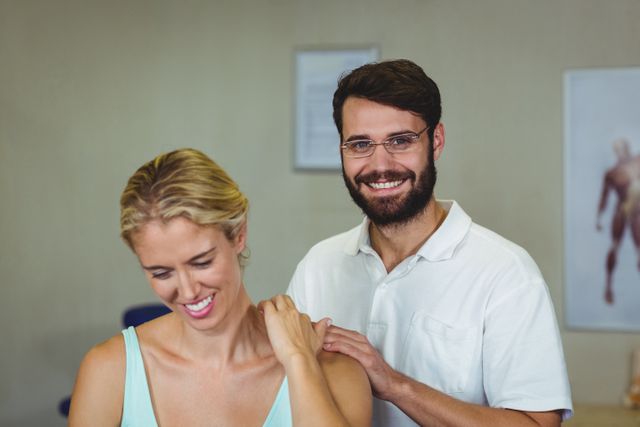 Male physiotherapist giving a neck massage to a female patient in a clinic. The physiotherapist is smiling, creating a welcoming and professional atmosphere. This image can be used for promoting healthcare services, physical therapy clinics, wellness centers, and rehabilitation programs. It highlights patient care, professional treatment, and the importance of physical therapy in maintaining health and wellness.