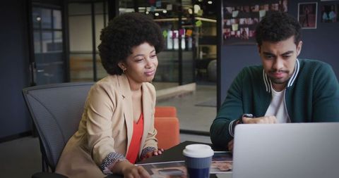 Diverse Coworkers Engaging in Laptop Discussion in Modern Casual Workspace