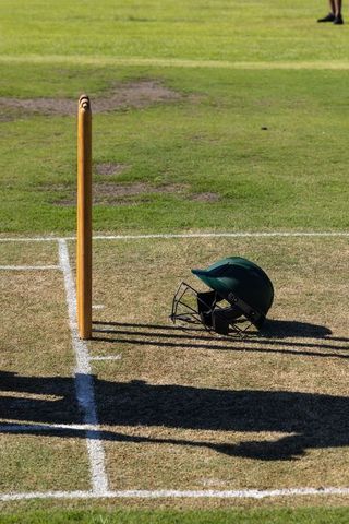 Cricket helmet beside stump on worn pitch with long shadows and white creases