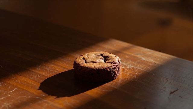 Golden hour chocolate chunk cookie on wooden table casting dramatic long shadow