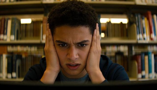 Male student holding head while studying on laptop in library, exam stress and focus