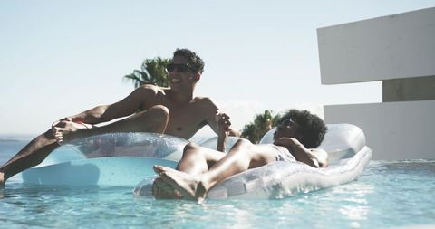 Rooftop infinity pool relaxing duo floating on transparent inflatable loungers by sea