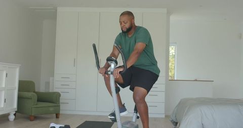 African man doing home cardio workout on stationary bike in bright minimal bedroom
