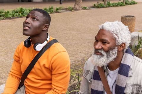 African american young and older men sitting on urban plaza ledge looking up, friendship