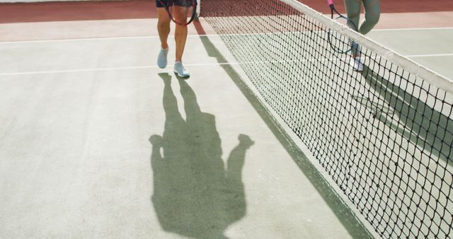 An image showing two tennis players shaking hands at the net after a match. This image can be used to illustrate themes of sportsmanship, competition, athletic events, and post-game appreciation in promotional materials, sports articles, and motivational content.