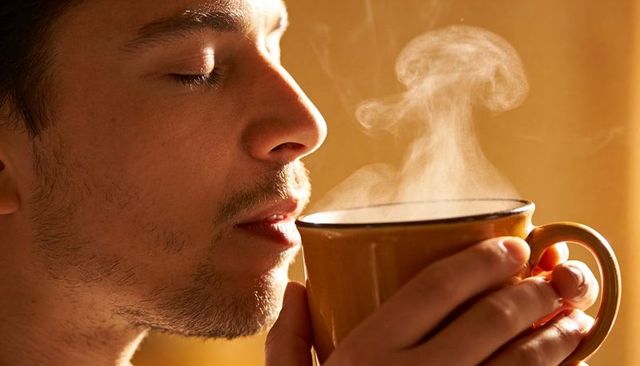 Young man inhaling steam from ceramic mug in warm golden light morning ritual