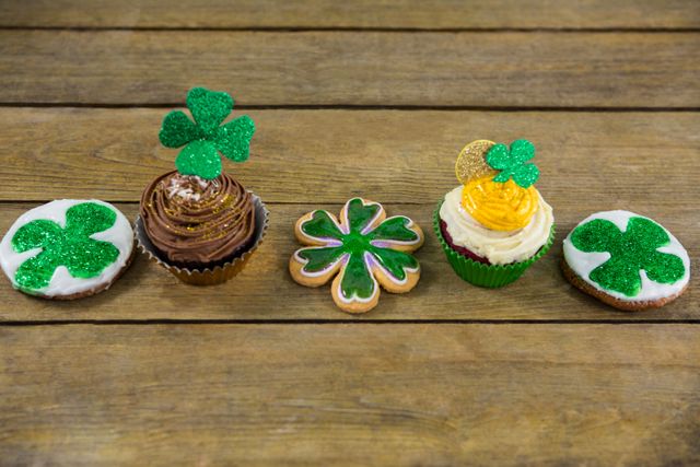 Festive St. Patrick's Day cupcakes and cookies decorated with green shamrocks on a wooden table. Ideal for holiday-themed promotions, baking blogs, festive party invitations, and Irish celebration advertisements.