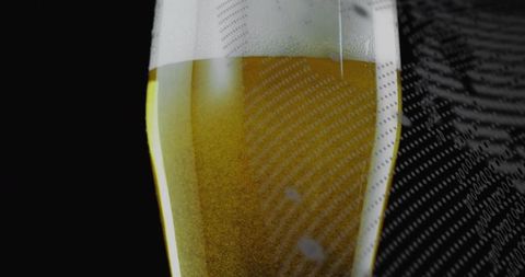 Gleaming tapered beer glass showcasing golden lager and frothy head with moody reflections