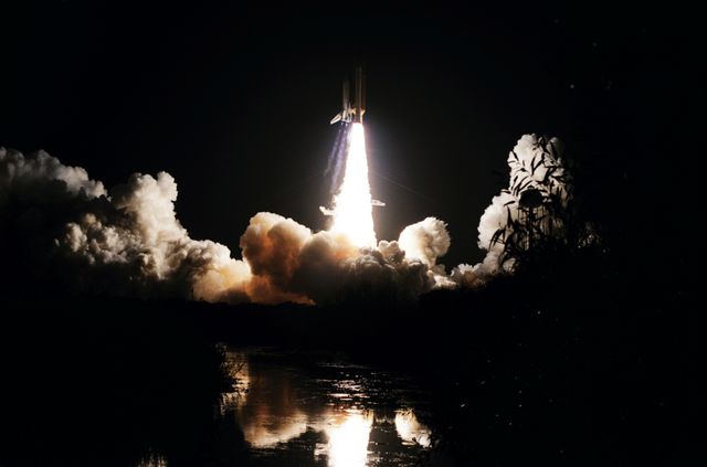 Dramatic image of Space Shuttle Discovery launching during dawn for the STS-51I mission on August 27, 1985. The reflection of the ignition in the nearby river amplifies the intensity of the scene. Suitable for use in articles on space exploration, technological advancements, NASA missions, and historical space launches.