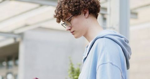 Teen student wearing blue hoodie using smartphone under modern campus canopy