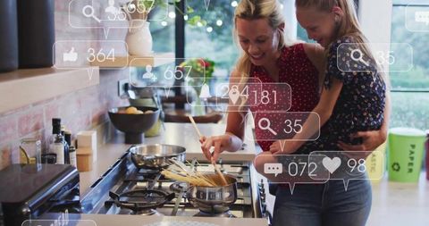 Mother stirring pasta while holding daughter in modern kitchen with social media icons
