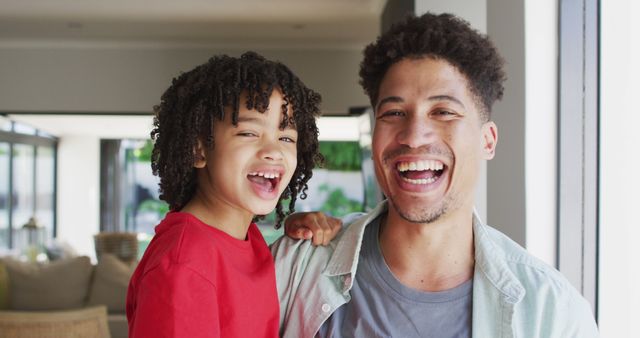 This heartwarming scene captures a father smiling with his son at home. Their joyous expressions showcase a strong familial bond and happiness. Great for use in family-related content, parenting articles, and advertisements promoting familial love and home life.