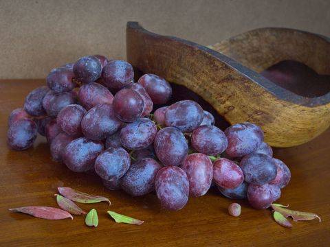 Fresh purple grapes with wooden bowl on rustic surface