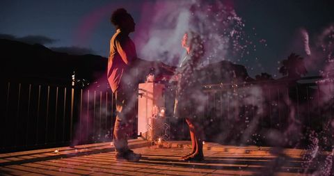 Romantic rooftop candlelit moment at dusk with couple holding hands and magenta haze