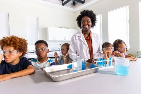 African american science teacher guiding young students wearing safety goggles in lab