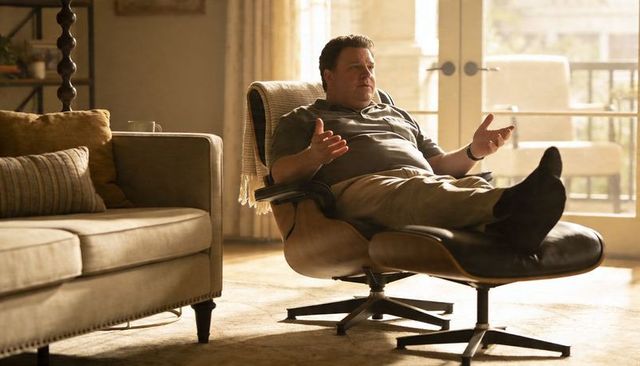 Reclining man gesturing in midcentury lounge chair, sunlit living room with balcony