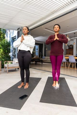 Diverse women practicing yoga and meditation on modern patio with mats and smartphone