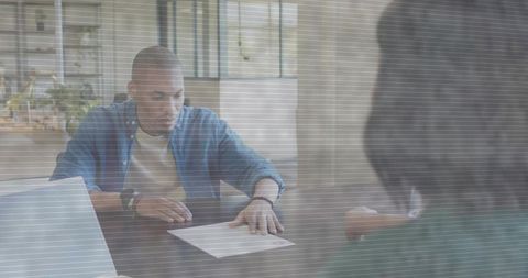 Young man reviewing contract at modern home office desk with laptop, colleague and plants