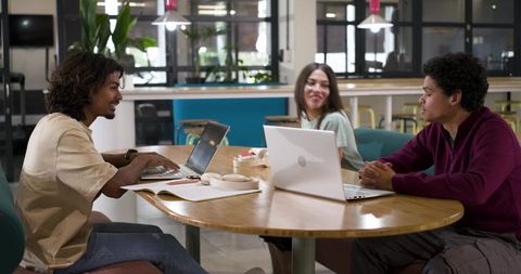 African American coworkers collaborating at round table in modern coworking space with laptops