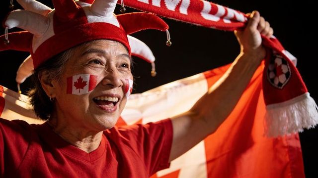 Senior asian fan cheering with canadian flag and red scarf in jester hat