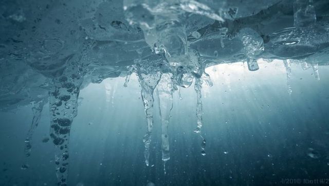 Melting icicles hanging beneath frozen lake with sunbeams penetrating icy water