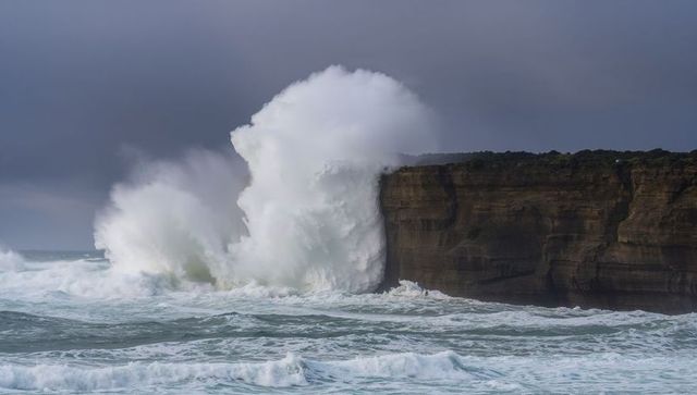 Giant ocean wave crashing against rocky cliff at stormy coastline