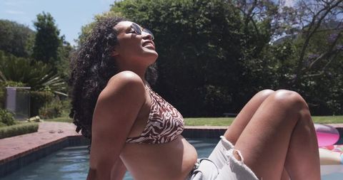 Sunlit backyard relaxation: african american woman sunbathing by pool in zebra bikini