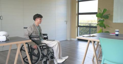 Young man in wheelchair participating in modern office meeting with vr headset nearby