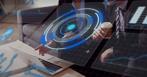 Business executives reviewing holographic data interface, pointing at laptop, holding coffee