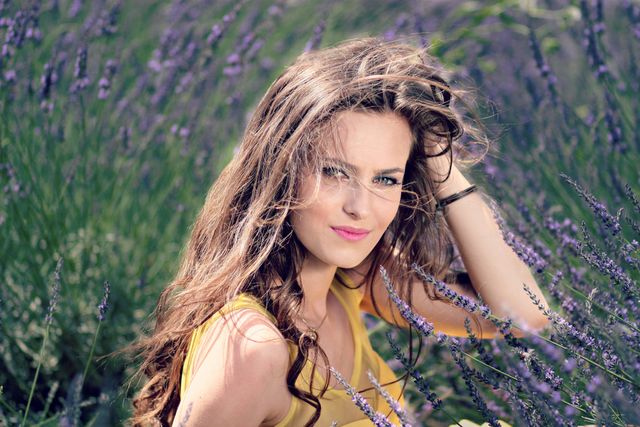 Women's Yellow Tank Top Holding Her Brown Curly Hair While Sitting on a Purple Flower - Download Free Stock Photos Pikwizard.com