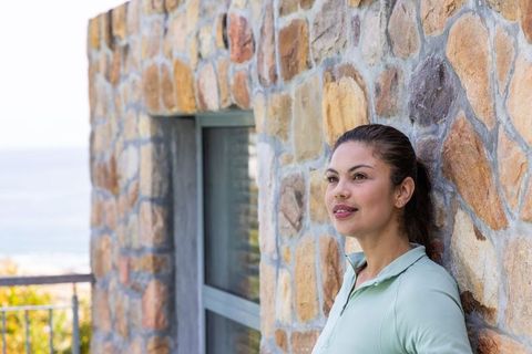 Serene woman leaning on textured stone wall overlooking sea from coastal terrace