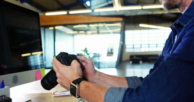 Professional photographer reviewing images on DSLR camera display at modern office workspace. Ideal for depicting creative industries, photography business, professional workspace, and technology in action.