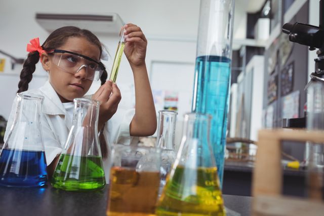 Elementary student examining yellow chemical in test tube by desk at science laboratory