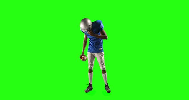 Football player wearing a uniform and helmet standing and posing with a football on a green screen background. This is ideal for graphic designers, videographers, and content creators looking for isolated sports elements to incorporate into their work or advertisements. The green screen allows for easy removal of the background for custom scenes and contexts.