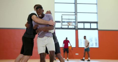 Young men celebrating on indoor basketball court hugging teammates in joyful team moment
