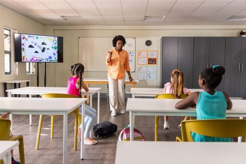 African American teacher leading engaging elementary kids in classroom with digital screen