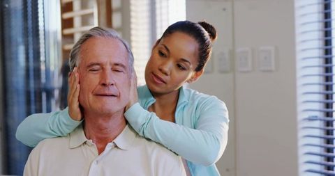 Homecare caregiver massaging senior man neck providing gentle therapy and relaxation