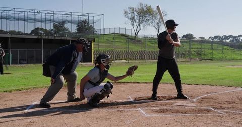 Batter preparing to swing while catcher squatting and umpire watching on sunny baseball field