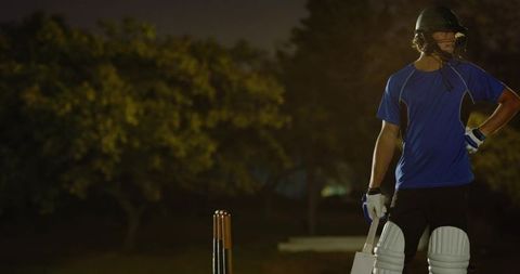 Teenage white cricketer holding bat on crease under floodlights preparing to face bowler