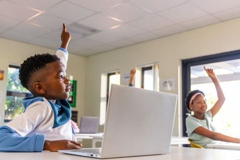 Raising hands during blended learning with laptop in bright elementary classroom