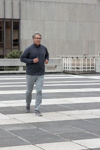 Senior man jogging on urban tiled plaza near concrete railing, minimalist monochrome