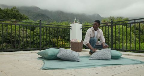 Man Arranging Cushions on Scenic Mountain Terrace for Relaxation