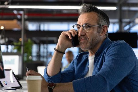 Mature professional consulting on phone while analyzing laptop charts in modern office