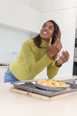 Asian woman presenting freshly baked pie, smiling while baking in modern bright kitchen