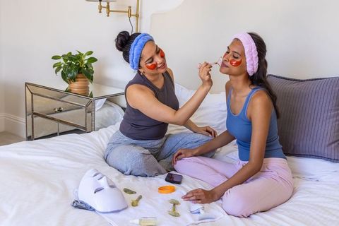 Two friends pampering with under-eye masks and jade rollers during at-home spa night