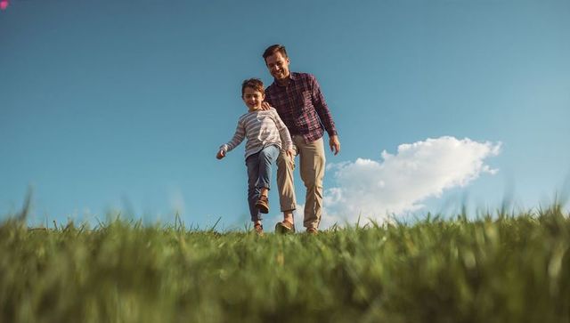 Father and son walking down sunny grassy hillside smiling together outdoor family bonding