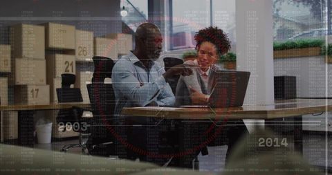 Mentor pointing and colleague reviewing laptop in coworking office with data overlay
