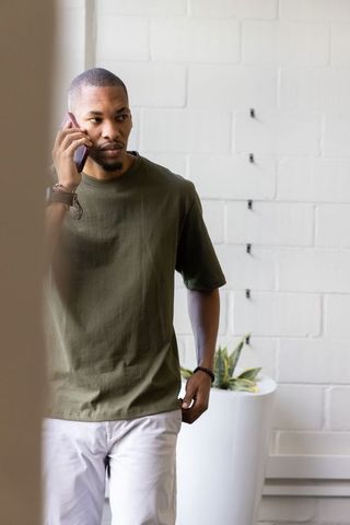 African american man talking on smartphone, standing and looking left in minimalist studio