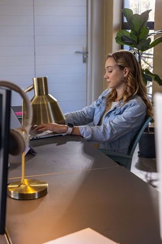 Young woman working at home office desk with laptop, brass lamp and smartwatch