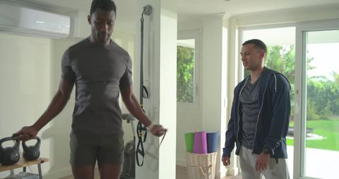 Black man jumping rope while caucasian trainer coaching in bright home gym